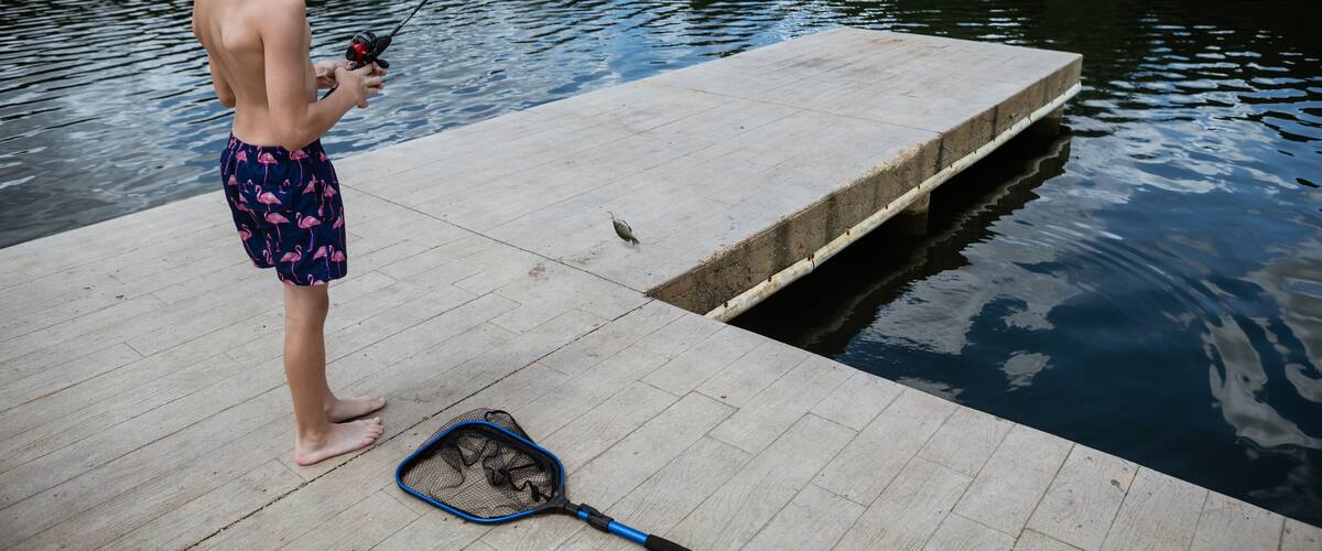 Boy reeling in small bluegill fish caught at lake