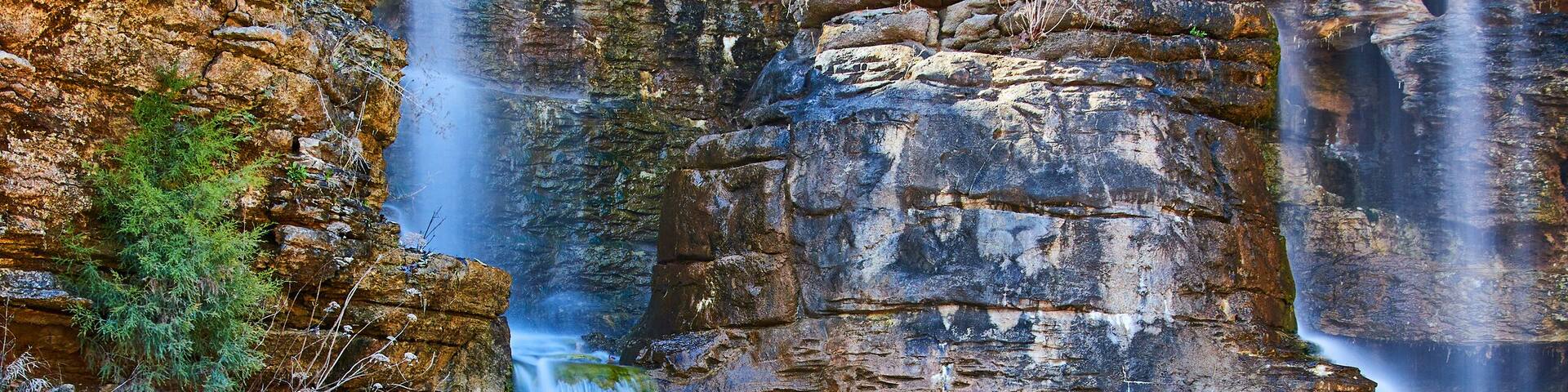Una cascada escalonada que se precipita sobre acantilados rocosos con una pasarela de madera cerca.