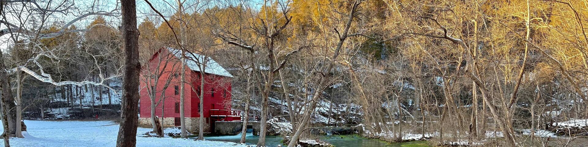 A river flowing through a snowy landscape with a red building and autumn-colored trees.