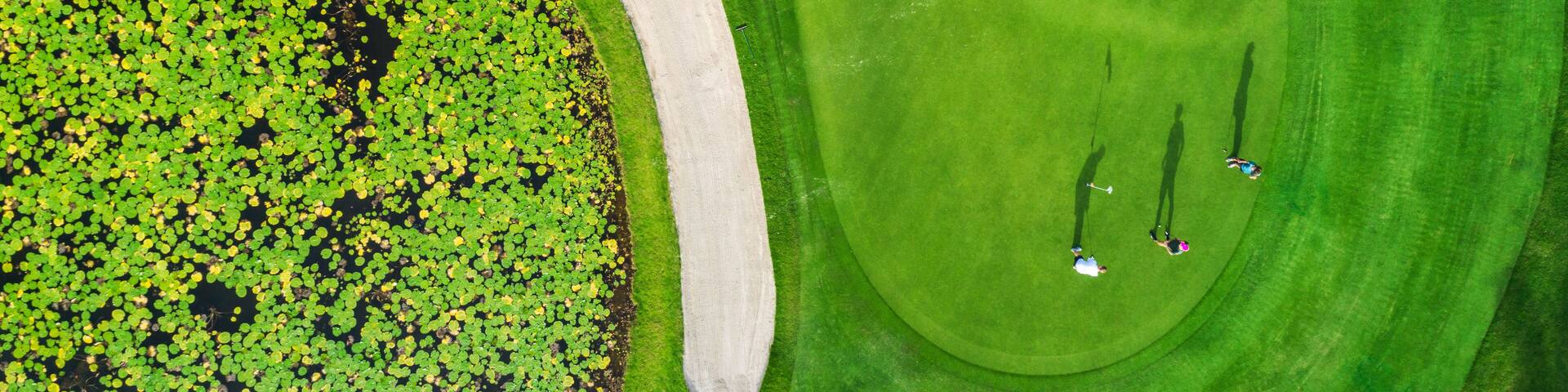 An aerial view of a golf course with a sand bunker, water hazards, and a putting green.