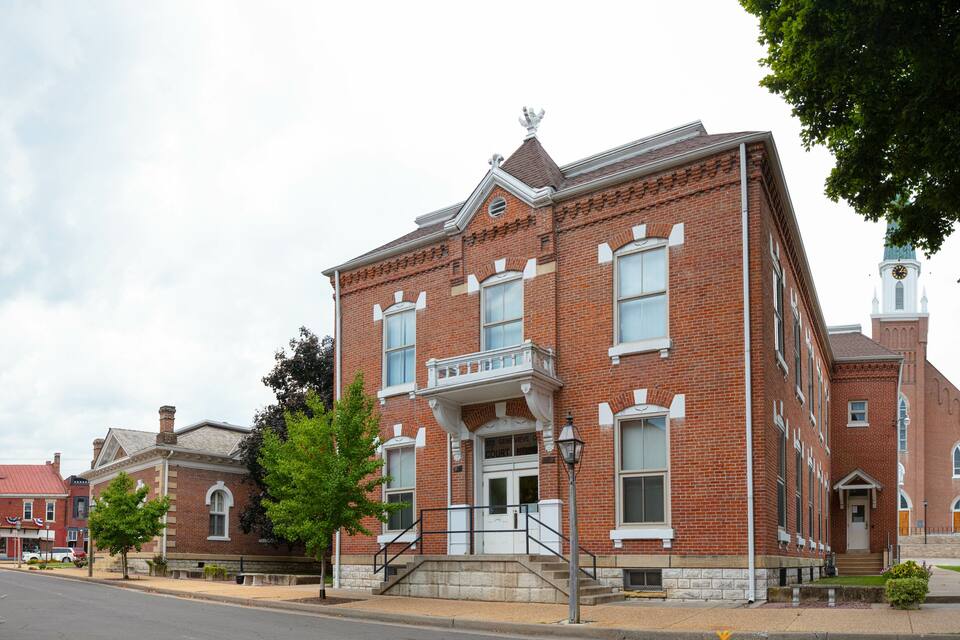 A historic red brick courthouse with a clock tower, surrounded by trees and a street.