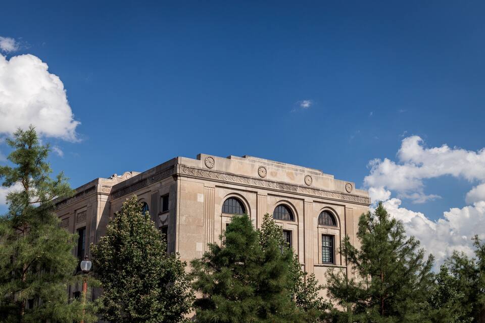 A historic building with arched windows and a clock tower, surrounded by trees.