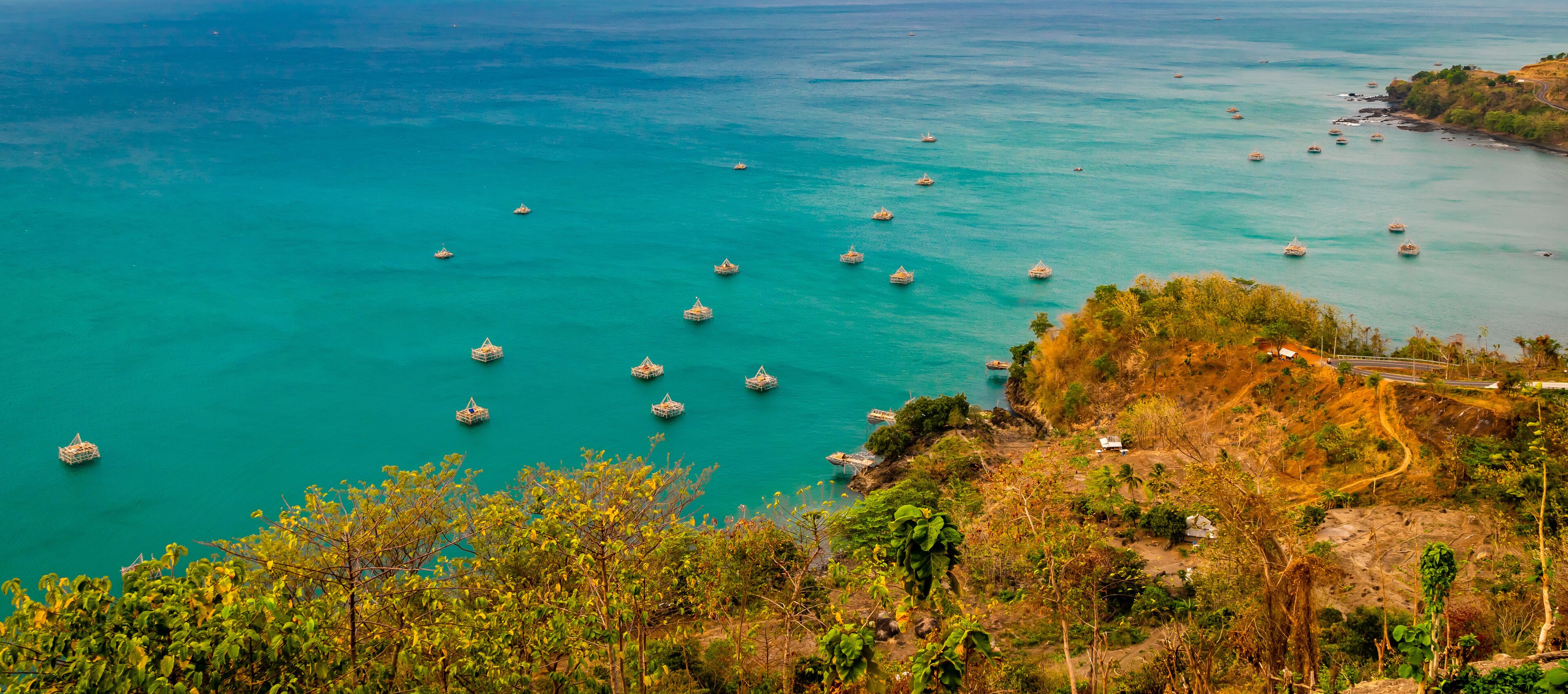 A coastal landscape with turquoise waters, numerous boats, and a hilly terrain with sparse vegetation.