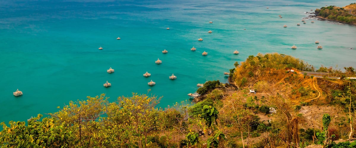 A coastal landscape with turquoise waters, numerous boats, and a hilly terrain with sparse vegetation.