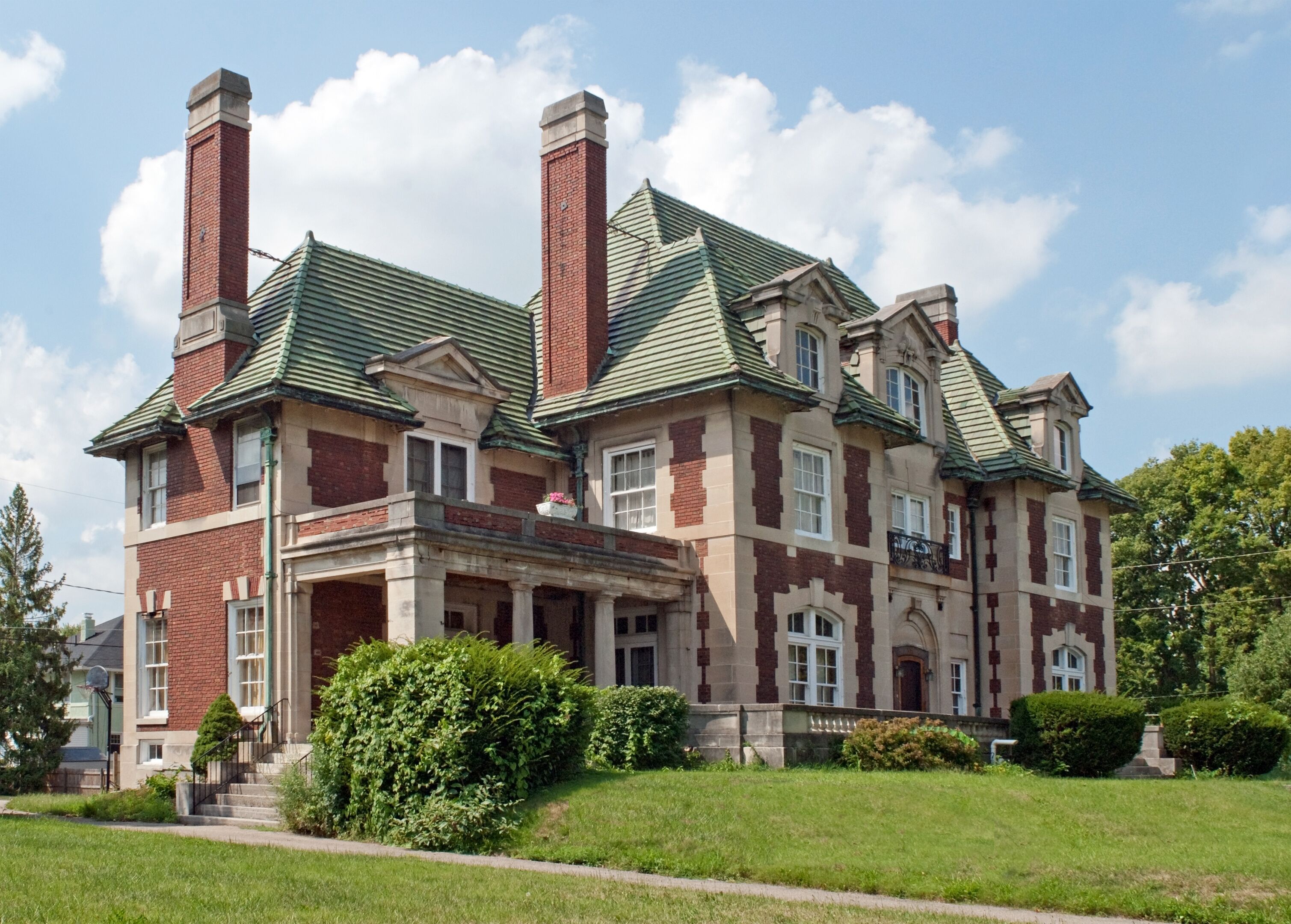 A large, historic house with a green roof, brick exterior, and multiple chimneys.