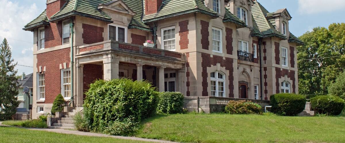 A large, historic house with a green roof, brick exterior, and multiple chimneys.