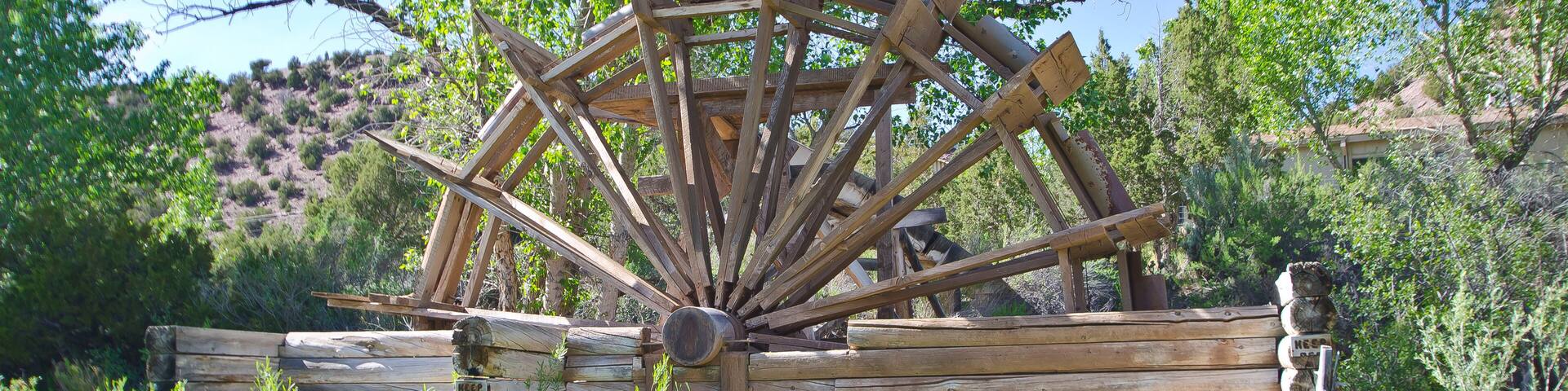 Une roue à eau en bois, située dans un environnement naturel, entourée de verdure et de collines.