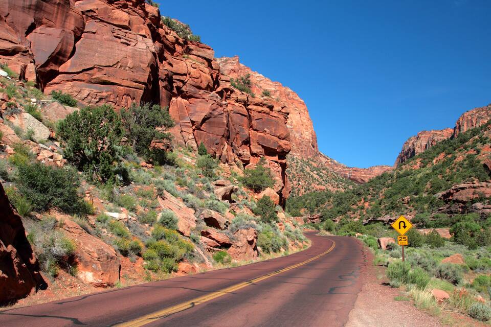 A winding road through a rocky canyon with red cliffs and sparse vegetation.