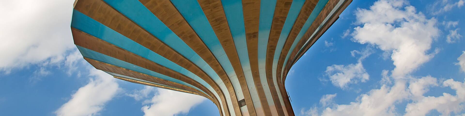 Una estructura grande y de forma peculiar con una combinación de colores azul y beige, sobre un cielo azul con nubes.