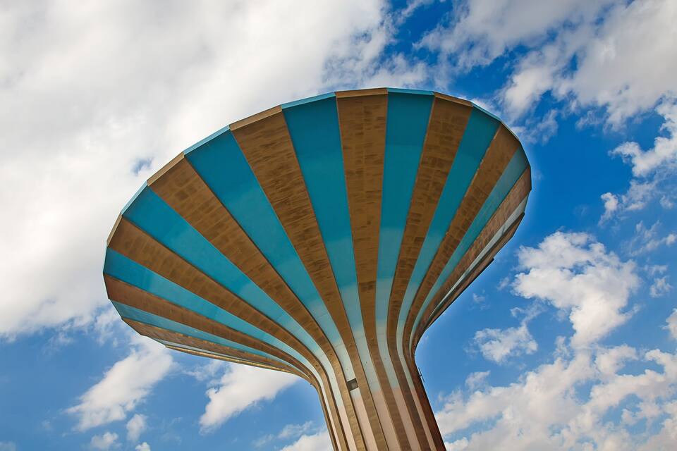 Una estructura grande y de forma peculiar con una combinación de colores azul y beige, sobre un cielo azul con nubes.