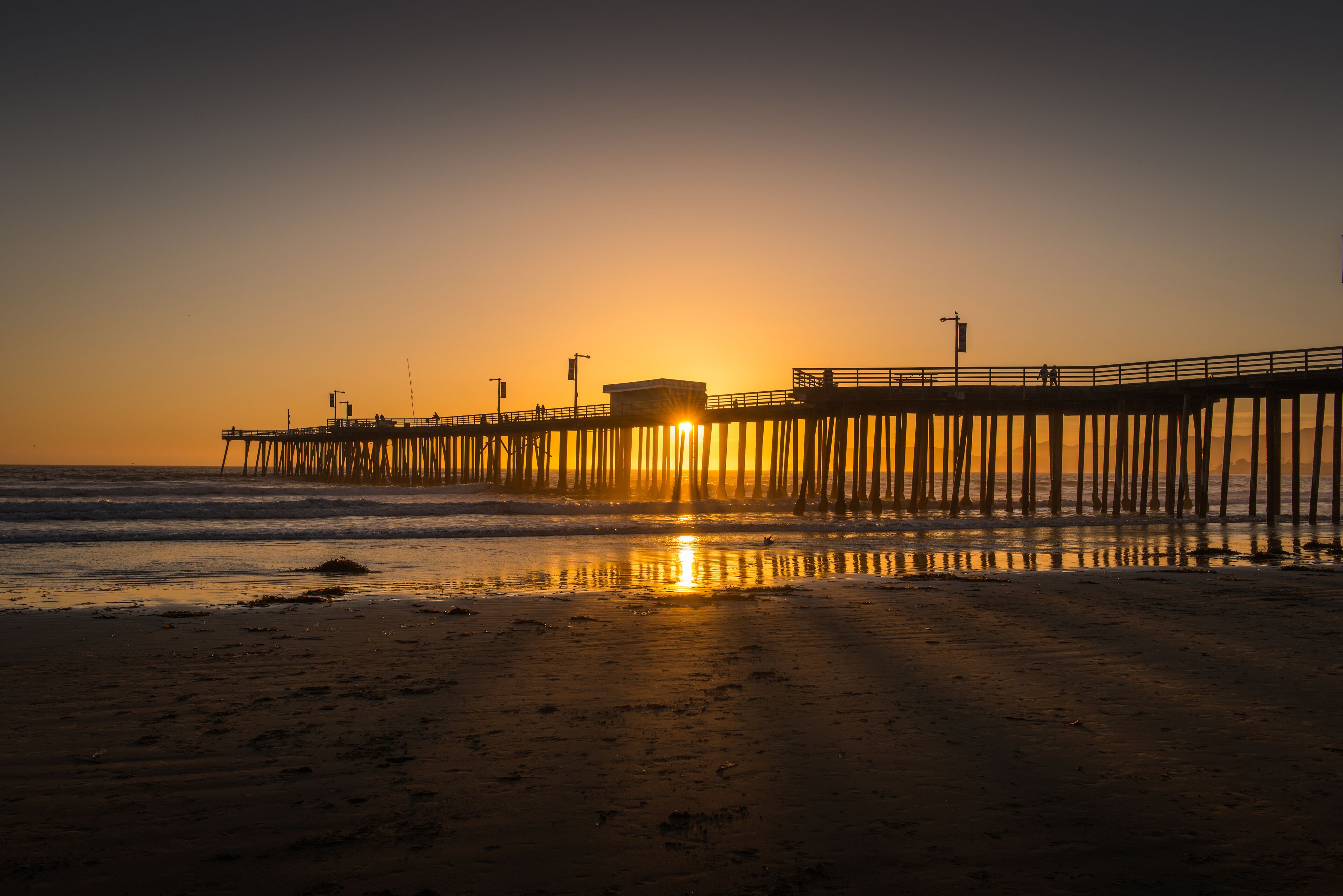 A pier extending into the ocean at sunset with the sun reflecting on the water.