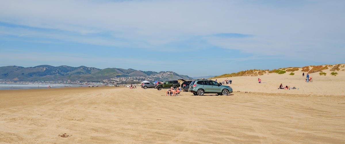A sandy beach with vehicles and people.