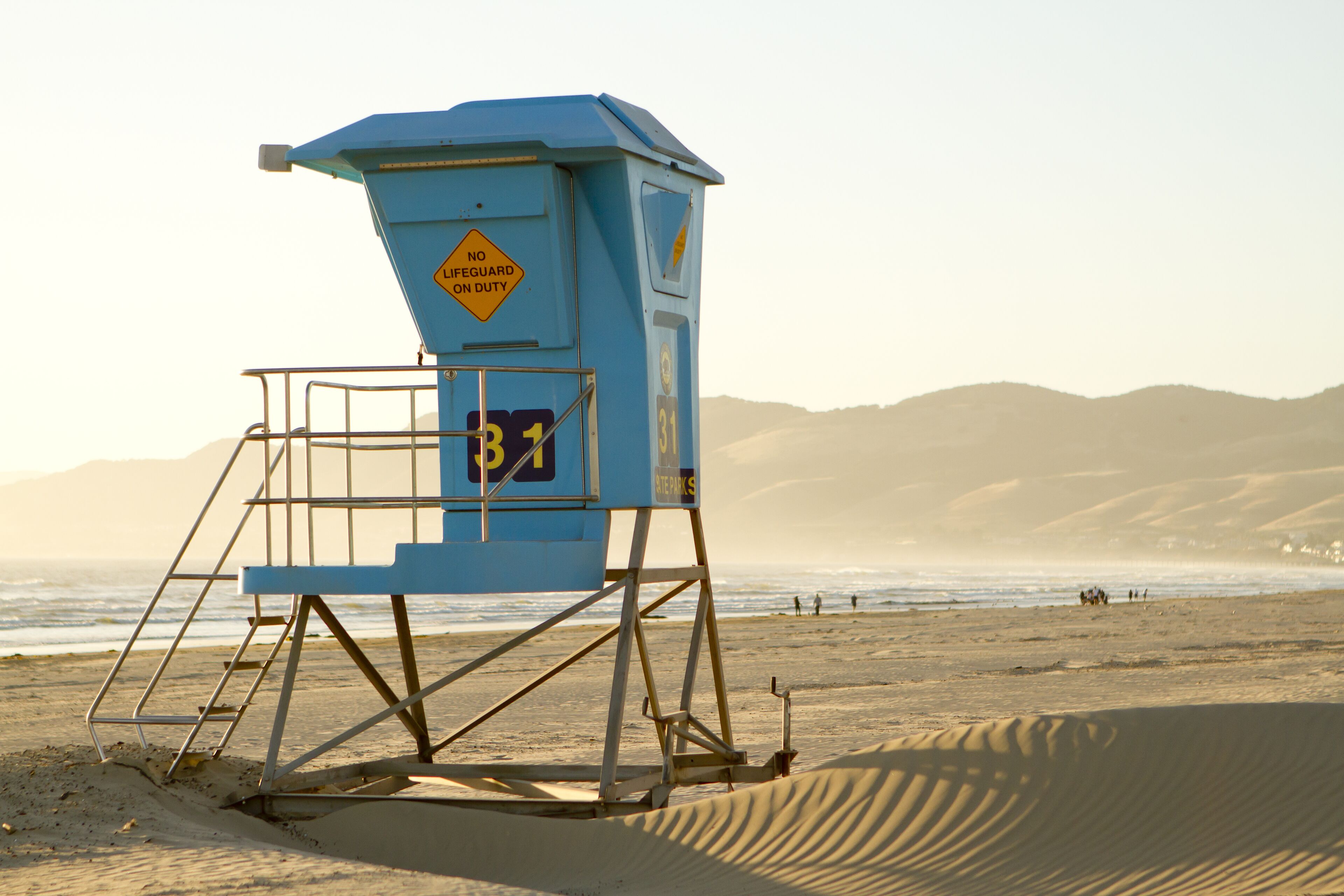 A lifeguard tower on a beach with a warning sign, a number 31, and a mountainous background.