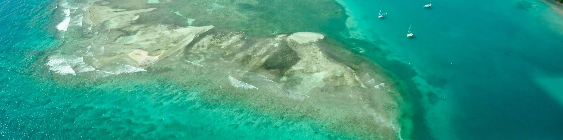 An aerial view of a turquoise coastal area with clear waters, several small islands, and boats anchored near the shore.