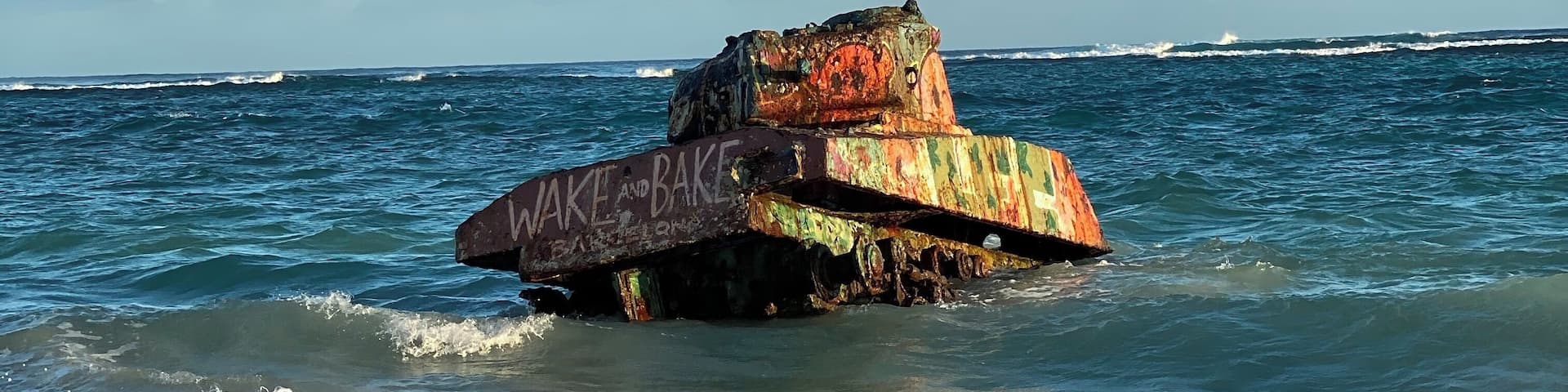 A rusted shipwreck with graffiti on its side, partially submerged in the ocean waves.