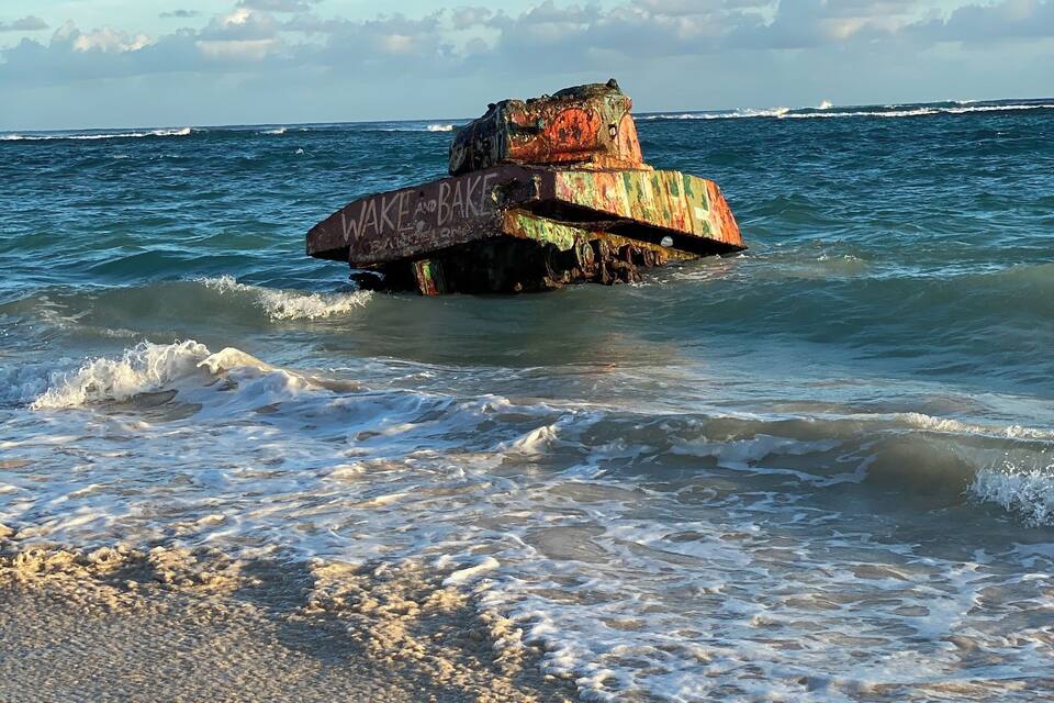 Nau naufrágada e enferrujada com pichações na lateral, parcialmente submersa nas ondas do oceano.