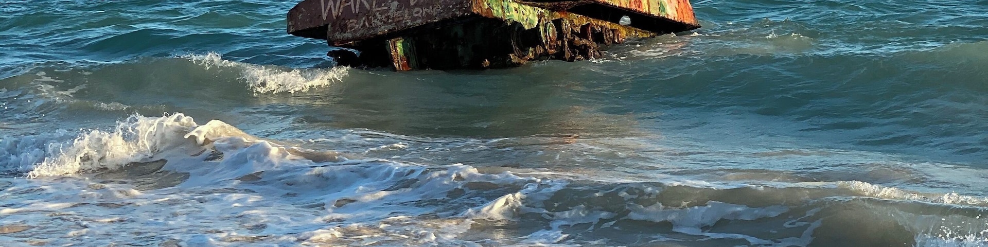 Un pecio oxidado con grafitis en su costado, parcialmente sumergido en las olas del océano.