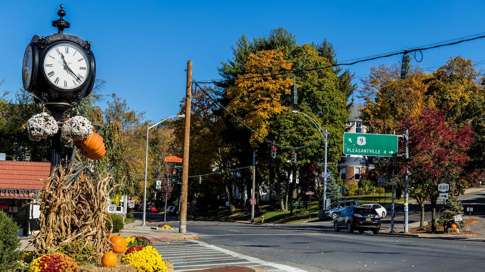 A town square with a clock, autumn foliage, and a street sign for Pleasantville.
