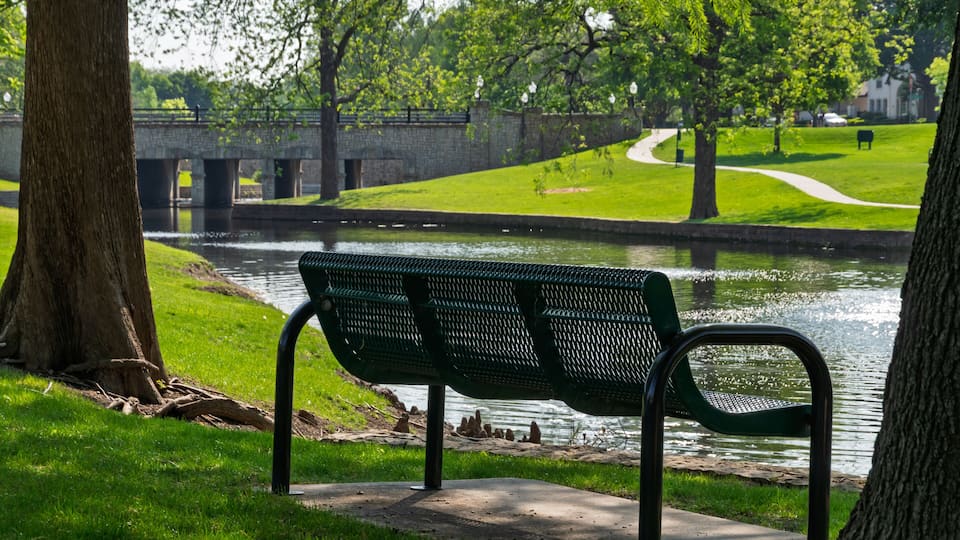 Empty park bench overlooking a calm pond and stone bridge