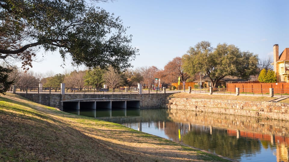 A calm river with a bridge, trees, and a stone wall.