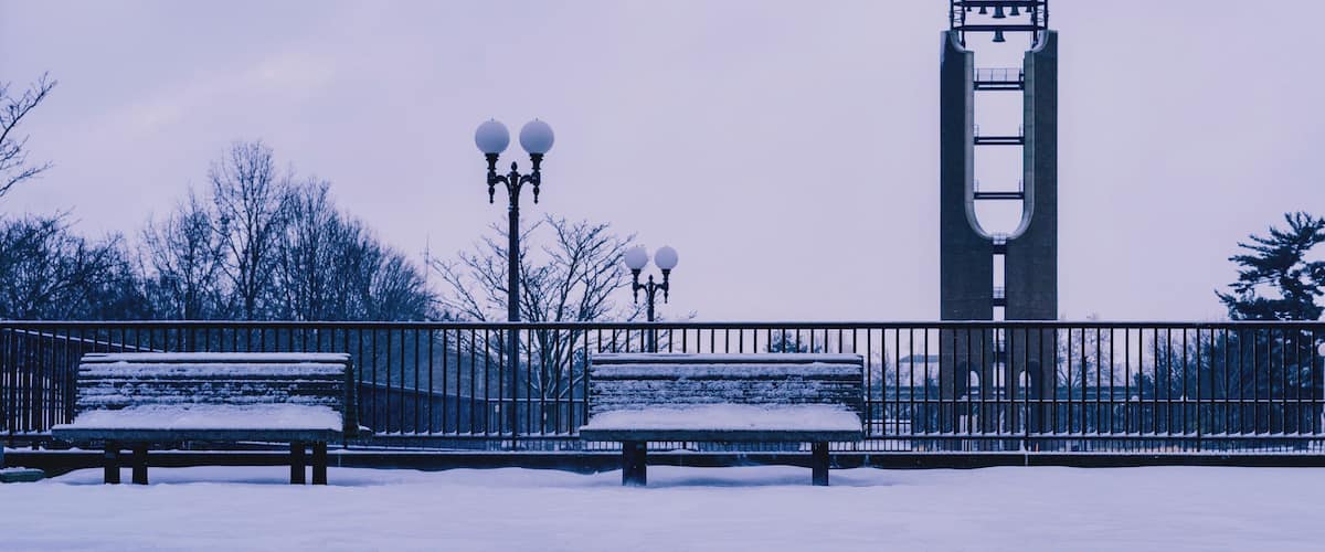A snow-covered bench, a metal fence, and a tower with a bell structure.