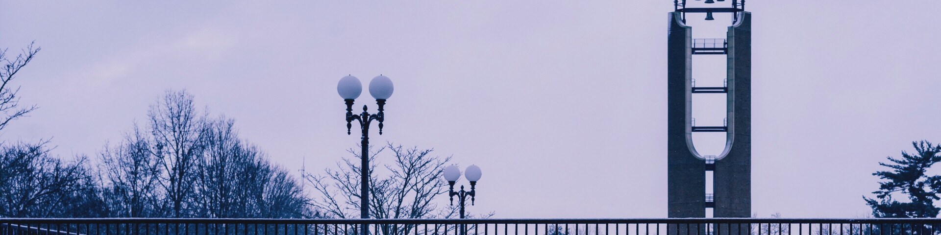 A snow-covered bench, a metal fence, and a tower with a bell structure.