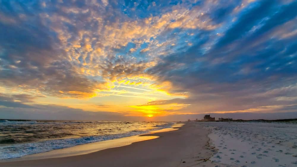 A beach with a sunset, ocean waves, and a distant city skyline.