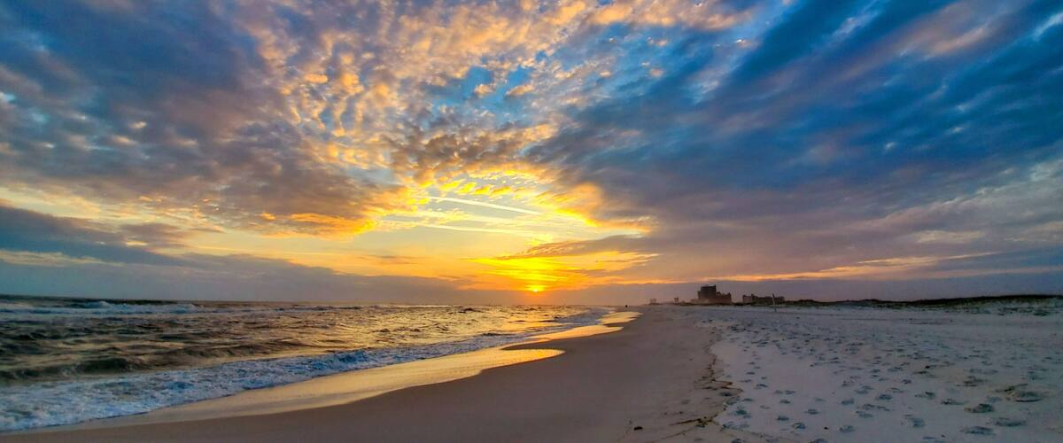 A beach with a sunset, ocean waves, and a distant city skyline.