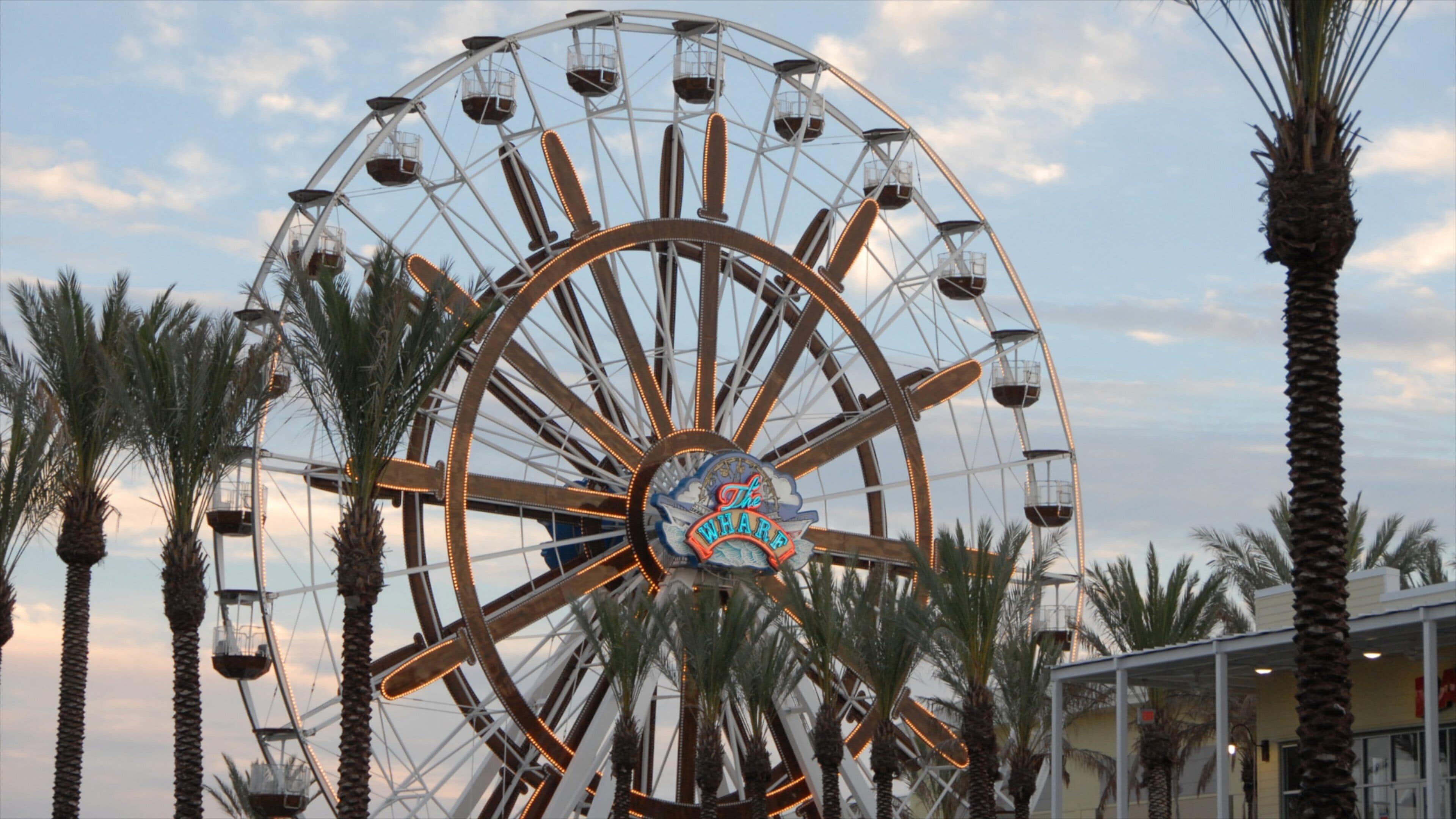 A large Ferris wheel with a sign that reads "The Wharf" surrounded by palm trees.