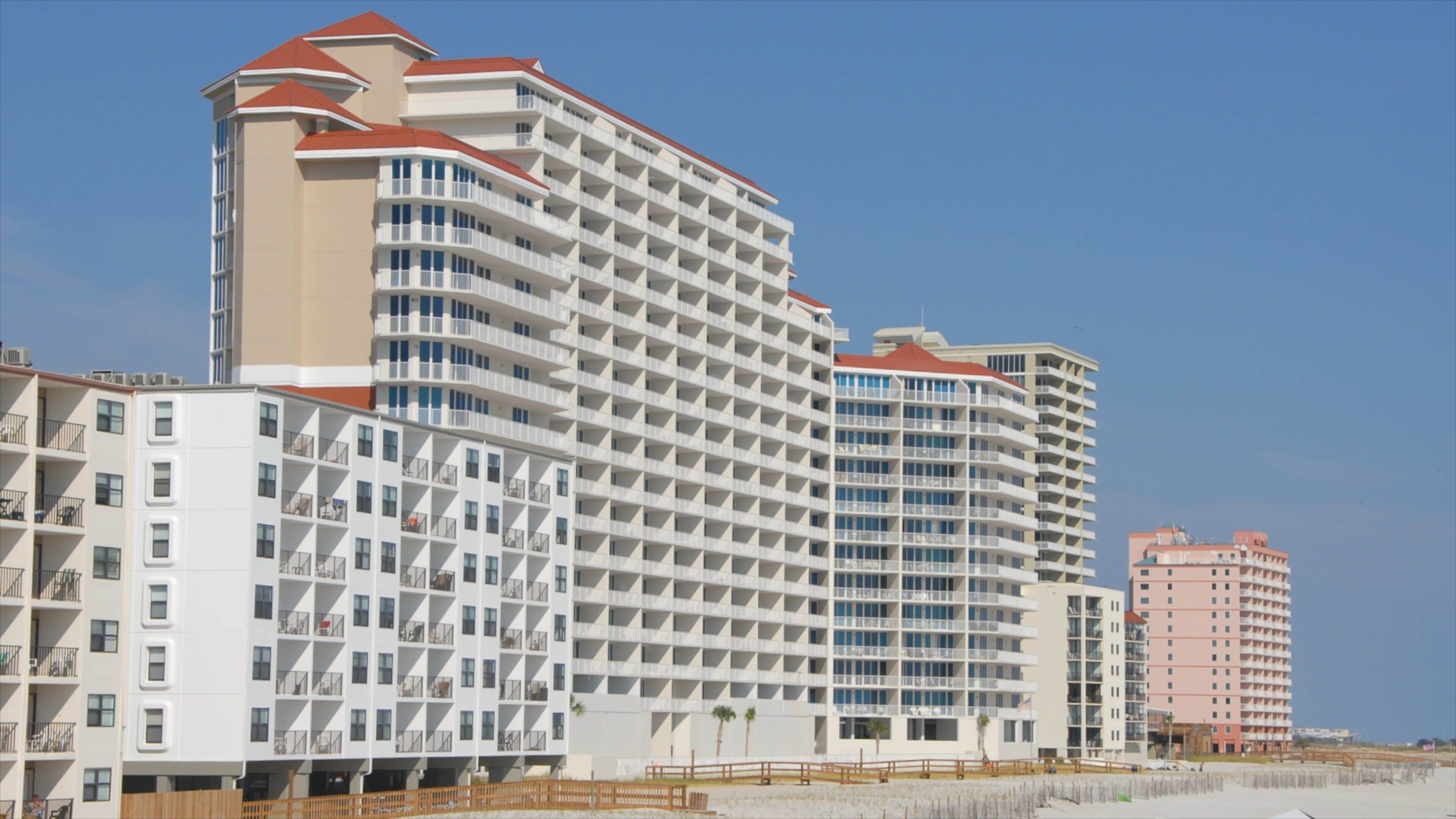 A beachfront hotel complex with multiple buildings, including a prominent white building with a red roof and a smaller pink building.