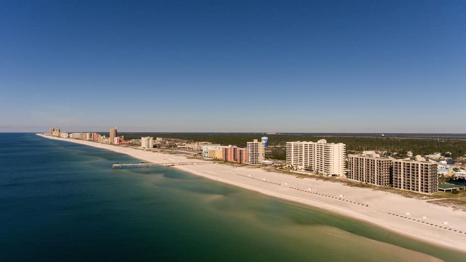 A coastal cityscape with a beach, high-rise buildings, and a clear blue sky.