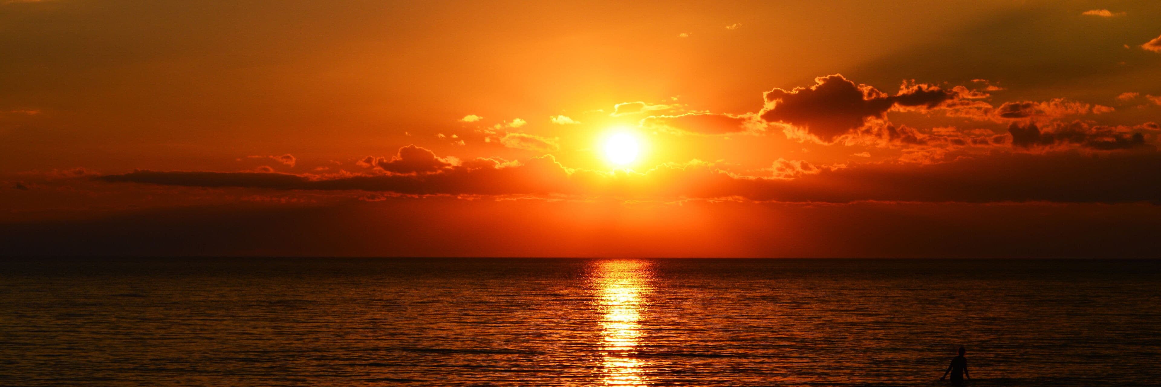 Um pôr do sol sobre o oceano, com a silhueta de uma pessoa em primeiro plano.