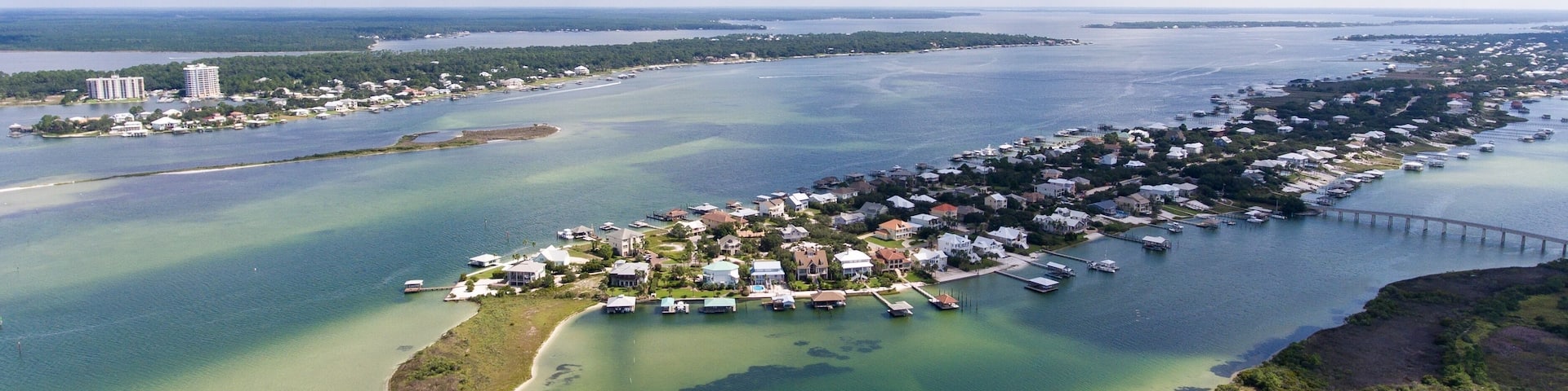 An aerial view of a coastal town with a marina, a bridge, and a clear sky.