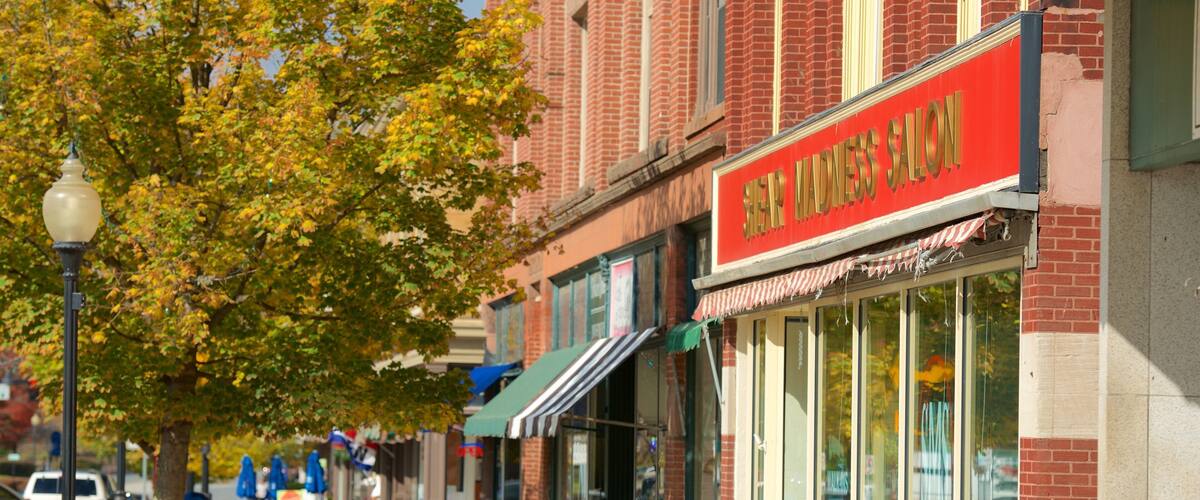 A street lined with brick buildings, one with a red awning and a sign reading "Shear Madness Salon".