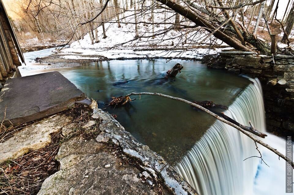 A waterfall in a forested area with snow on the ground.