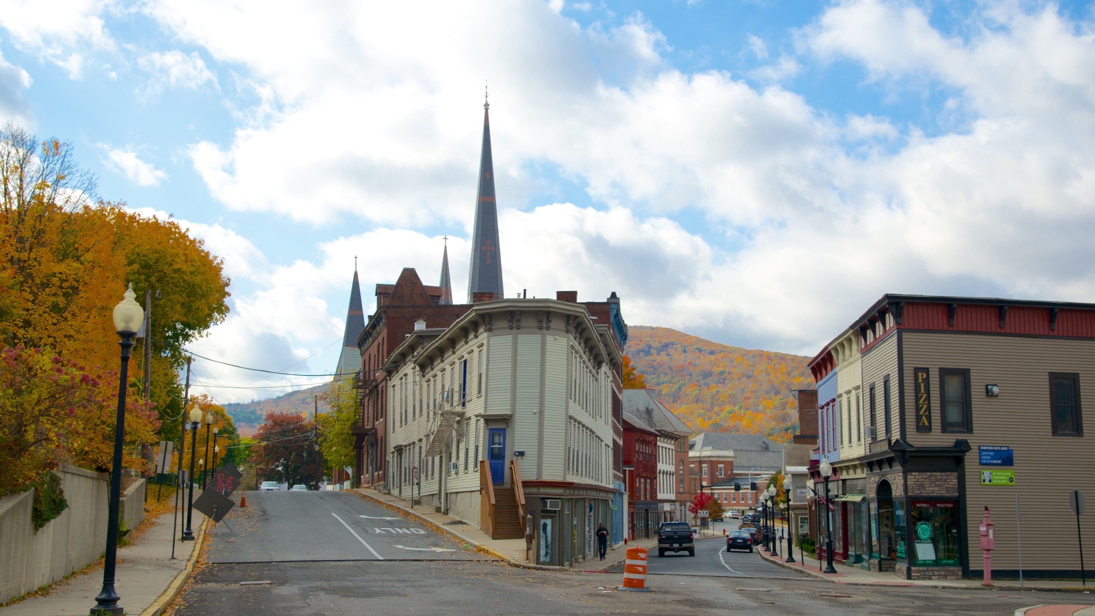 A street with autumn foliage, a church spire, and a pizza shop.