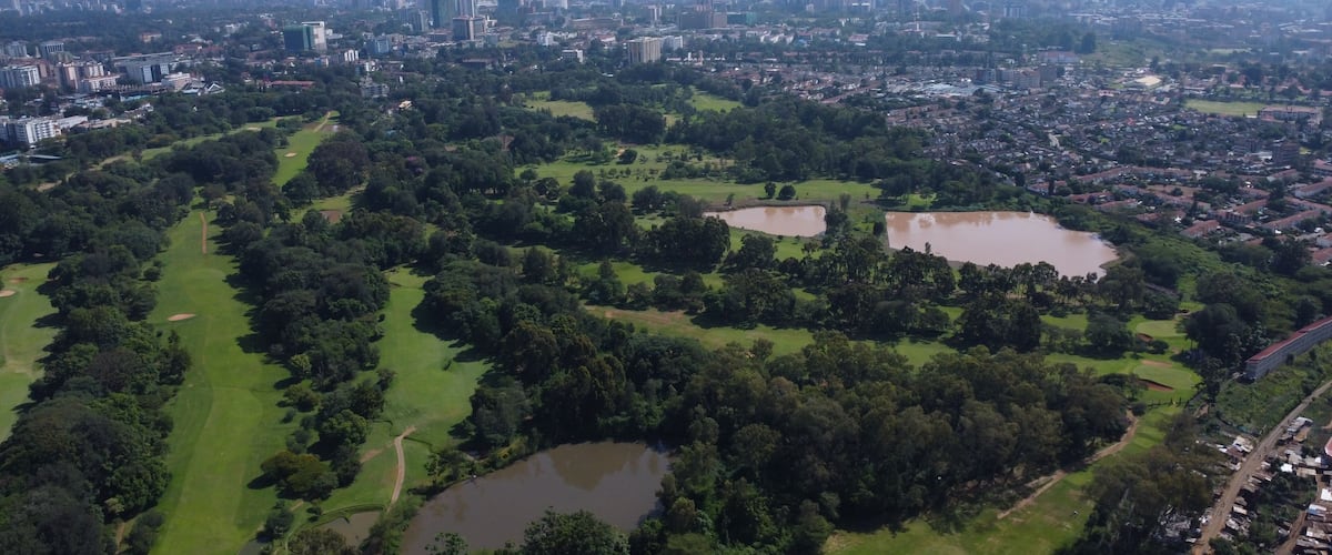 Aerial view of a golf course with ponds and a sprawling city skyline in the background.