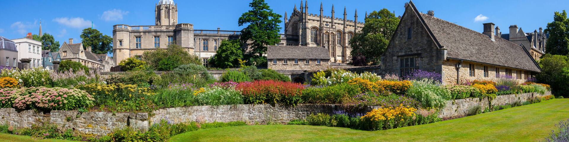 A historic building with a tower, surrounded by a well-maintained garden with various colorful flowers and a stone wall.