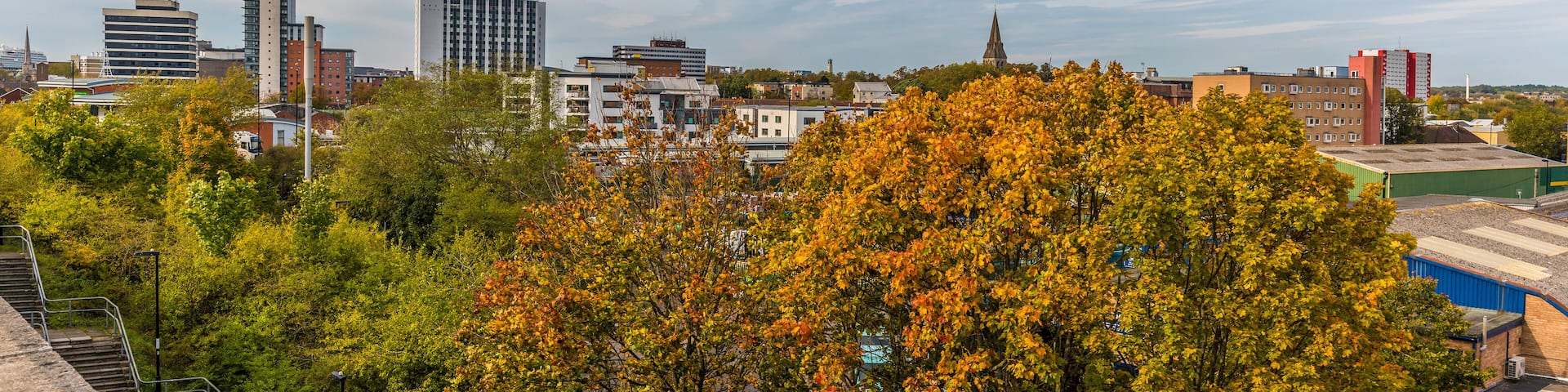 A cityscape with autumn foliage, modern buildings, and a church spire.