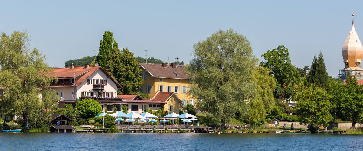 A lakeside town with colorful houses, a church steeple, and a dock with boats.