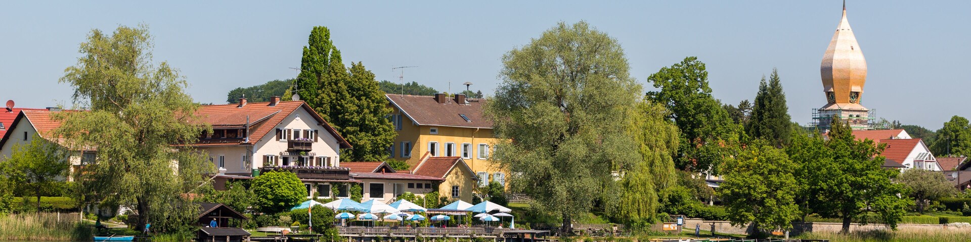 A lakeside town with colorful houses, a church steeple, and a dock with boats.
