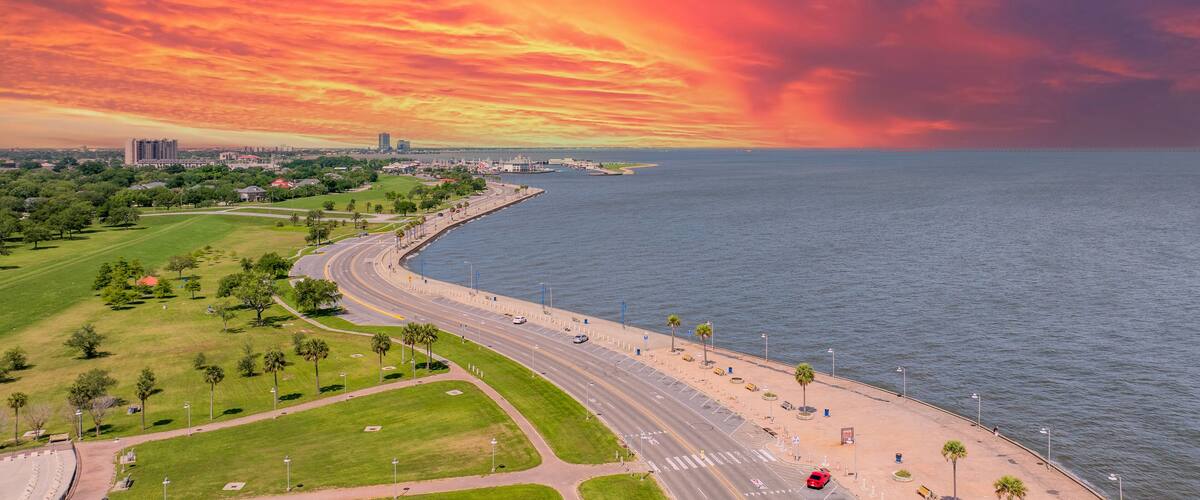 Aerial shot along the coast of Lake Pontchartrain with office buildings and lush green trees and grass at Lakeshore Park in New Orleans Louisiana USA