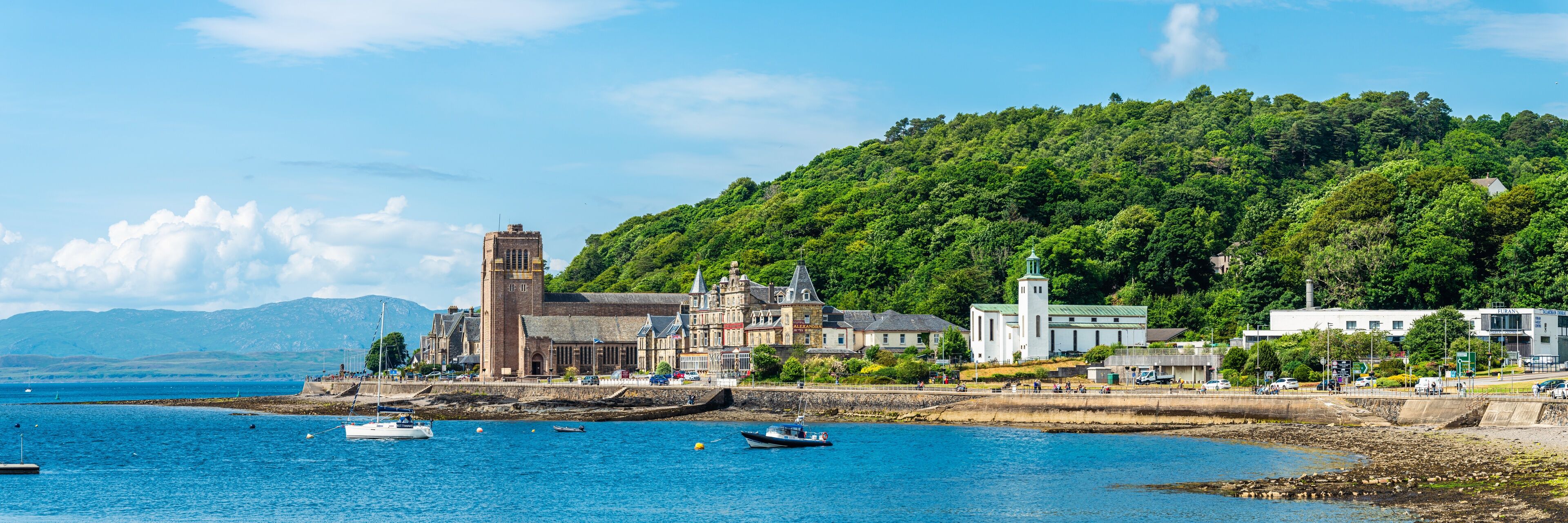 A coastal town with a historic building, a church, and a hill with dense greenery.