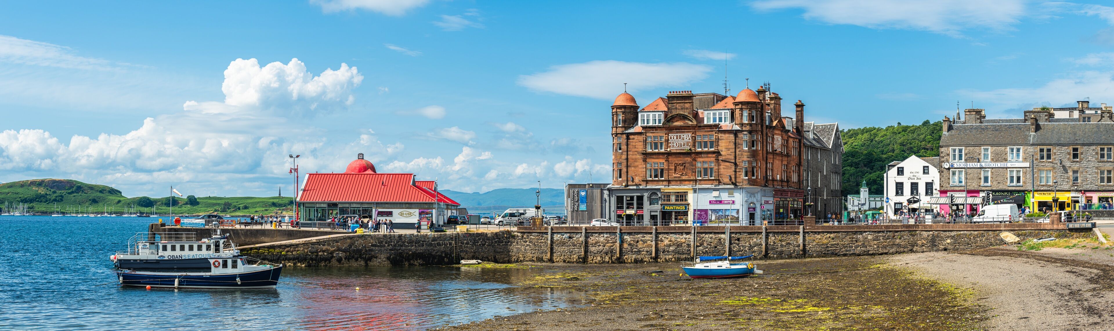 A coastal town with a prominent red-roofed building, a historic stone building, and a pier with boats.