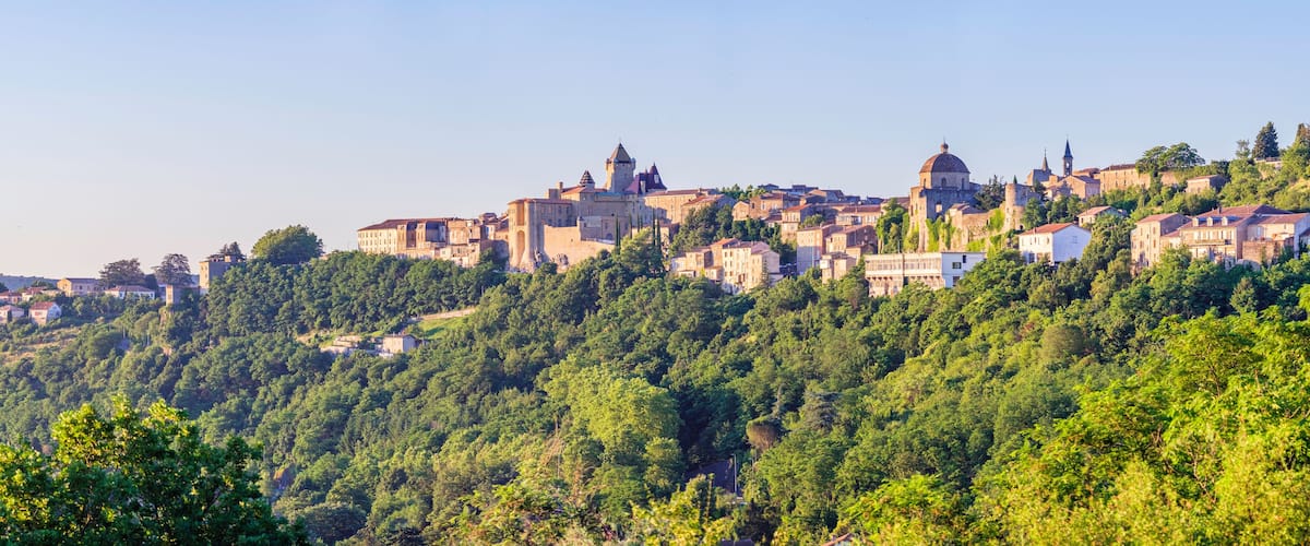 A historic town perched on a hillside with dense forest, medieval architecture, and a prominent church tower.
