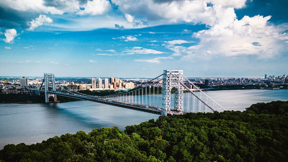 A suspension bridge over a river with a cityscape in the background.