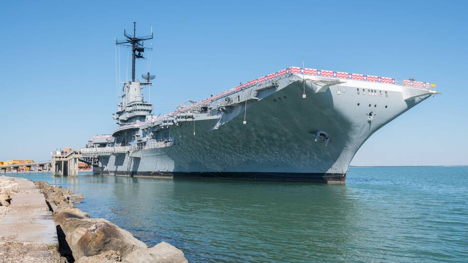 A large naval ship docked at a pier with a clear sky.
