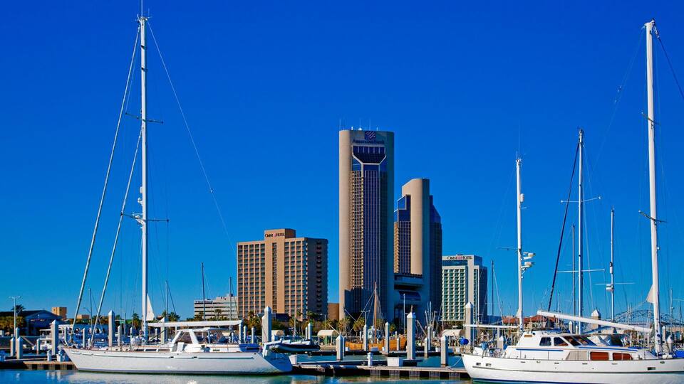 A marina with several yachts docked, a tall building with 'CNN' signage, and other high-rise buildings in the background.