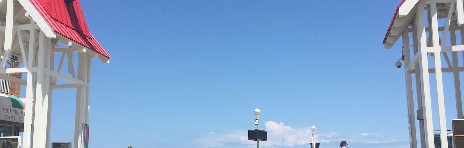 Un cielo azul despejado con un letrero que dice "Boardwalk Ocean City Maryland" y gente caminando por la pasarela.