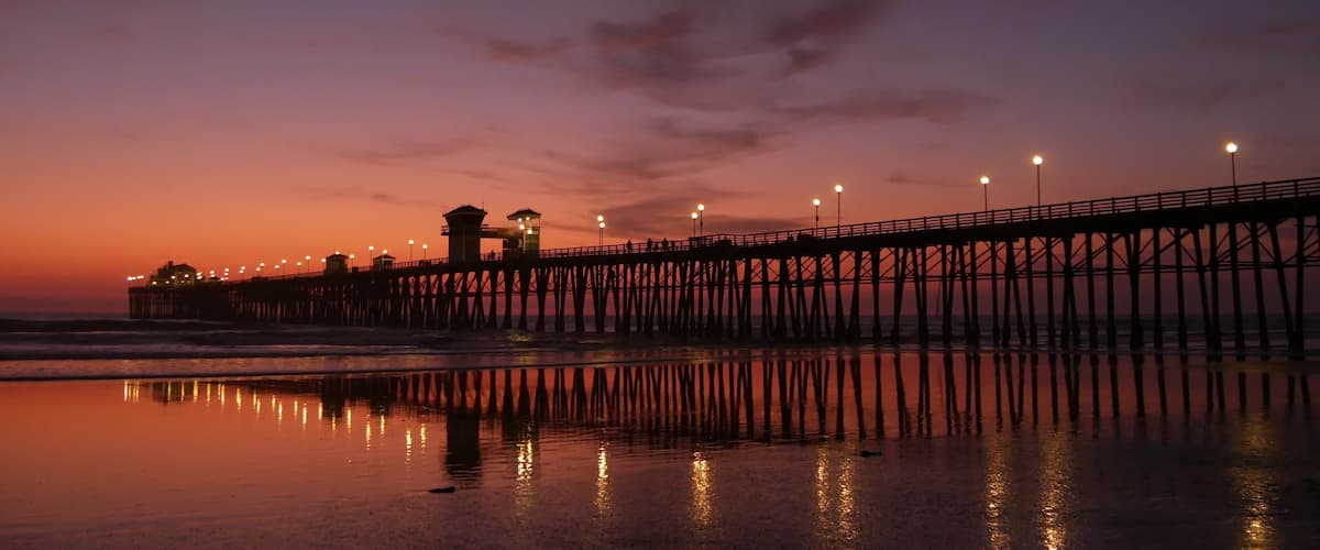 A pier extending into the water at sunset with lights along its length and a building on the left.
